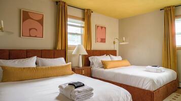 A hotel room with two beds, a nightstand, a lamp, and artwork on the walls.