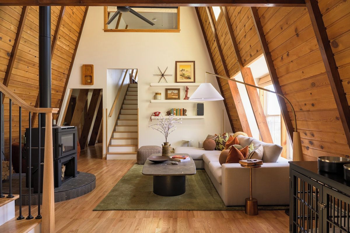A loft-style room with a wooden ceiling, a fireplace, a sofa, a coffee table, and a staircase.