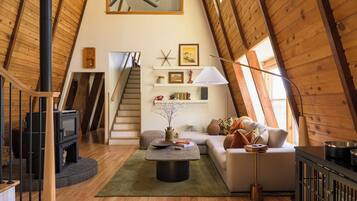 A loft-style room with a wooden ceiling, a fireplace, a sofa, a coffee table, and a staircase.