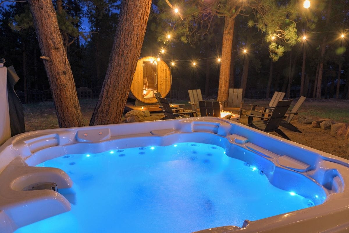 A hot tub with a blue light, surrounded by trees and outdoor furniture.
