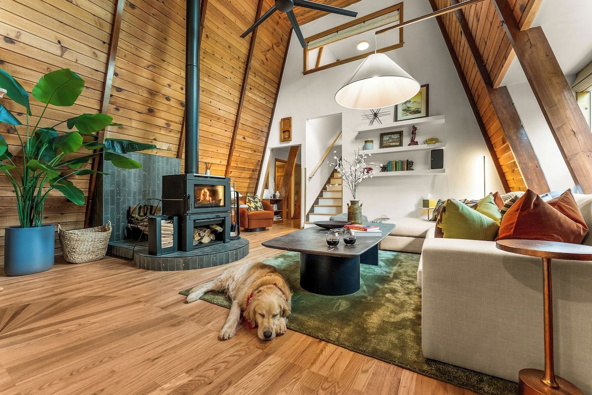 A cozy loft-style living space with a wooden ceiling, a fireplace, a sofa, a coffee table, and a dog resting on the floor.