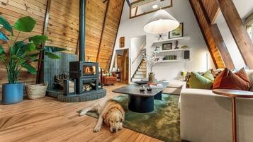 A cozy loft-style living space with a wooden ceiling, a fireplace, a sofa, a coffee table, and a dog resting on the floor.