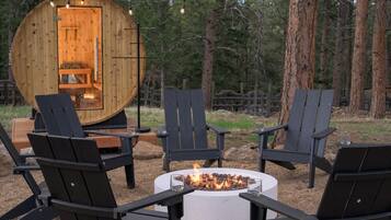 A wooden cabin with a circular interior, surrounded by outdoor seating and a fire pit.
