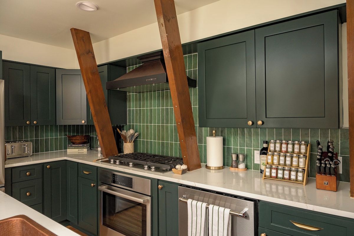 A modern kitchen with dark green cabinets, a stainless steel range, and a wooden beam ceiling.