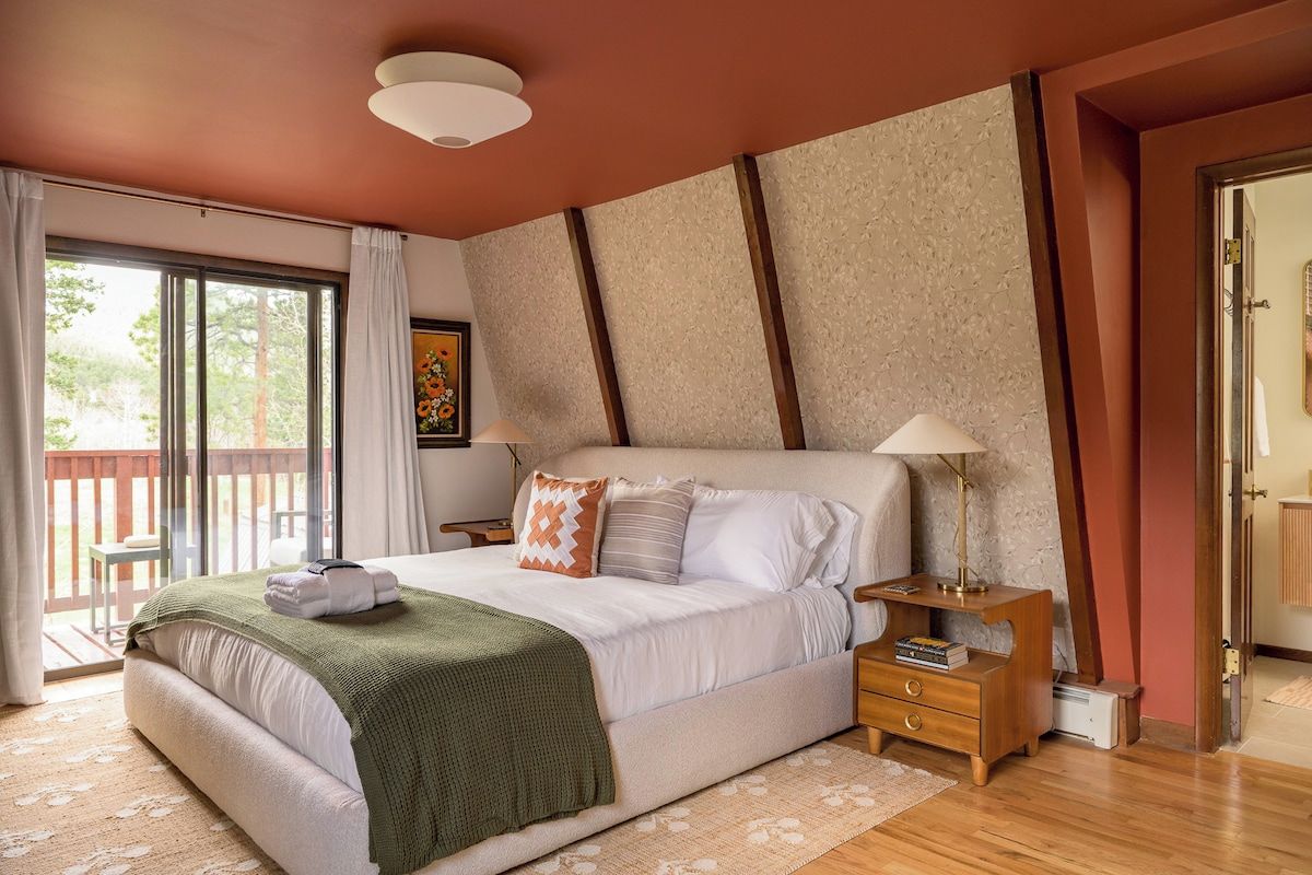 A bedroom with a large bed, a nightstand, a lamp, and a view of the outdoors.
