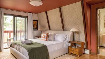 A bedroom with a large bed, a nightstand, a lamp, and a view of the outdoors.