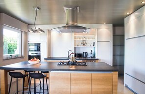 Una cocina moderna con una isla central, taburetes de bar, hervidor y electrodomésticos integrados.