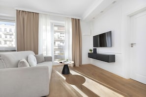 Ein modernes Wohnzimmer mit einer Couch, einem Couchtisch, einem an der Wand montierten Fernseher und Blick auf die Stadt durch große Fenster.