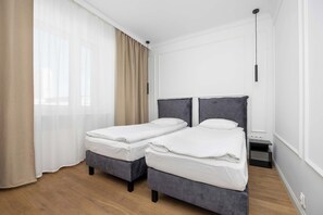 A hotel room with two single beds, a wooden floor, a window with sheer curtains, and a nightstand with a lamp. - Warsaw | Marszałkowska 83 | Spacious apartment | 2 bedrooms (Warszawa)
