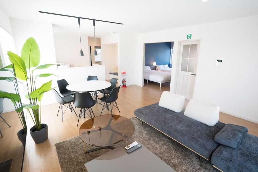 A modern hotel room with a sofa, a round table with chairs, a potted plant, and a bed with a view.