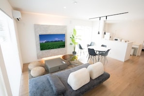 Ein modernes Wohnzimmer mit einer Couch, Hocker, einem Couchtisch und einem an der Wand befestigten Flachbildfernseher.