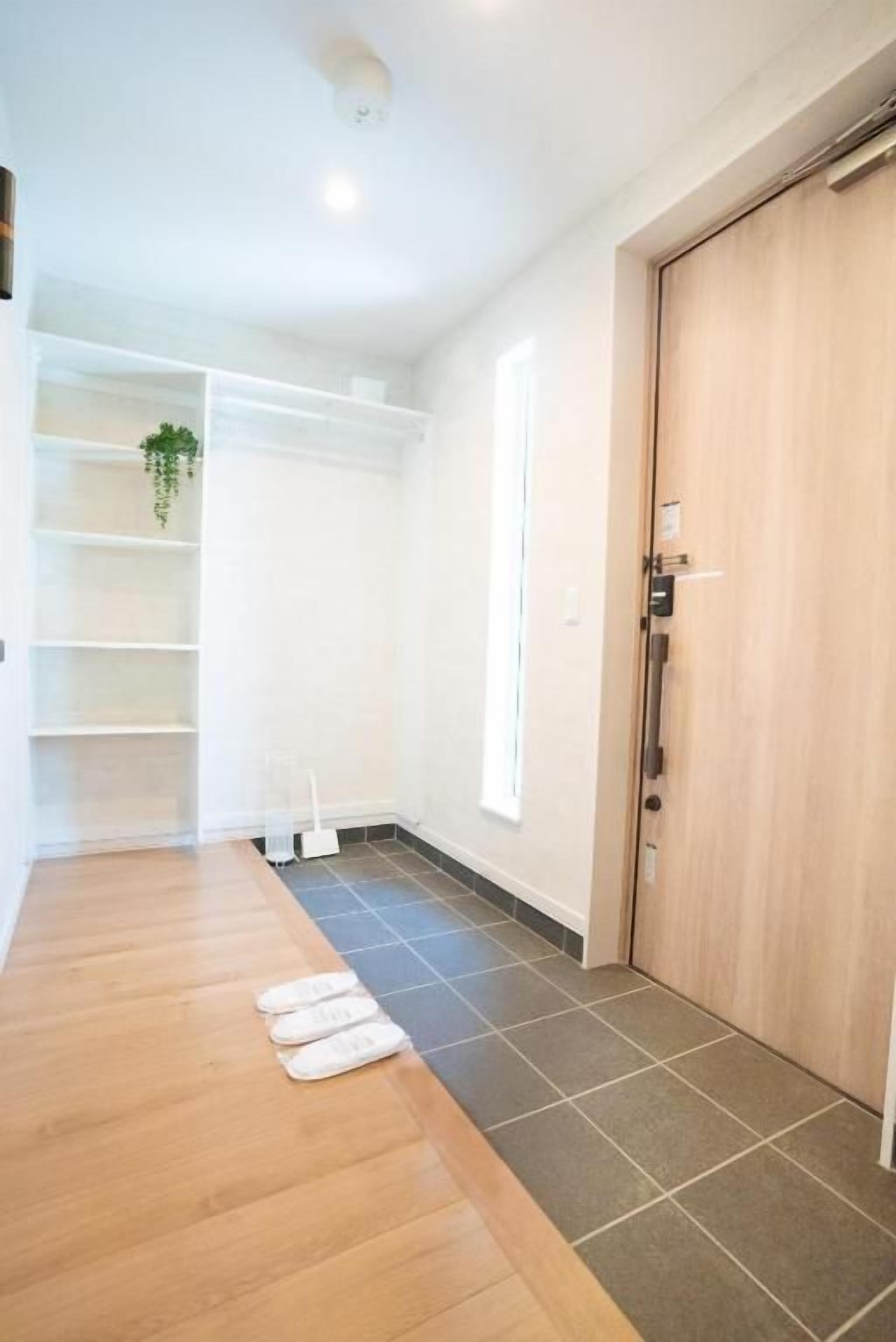 A hallway with a wooden floor, a white wall, a door, and a shelf with a plant.