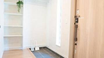 A hallway with a wooden floor, a white wall, a door, and a shelf with a plant.
