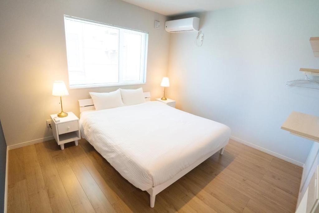 A bedroom with a bed, two bedside tables with lamps, a window, and an air conditioning unit.