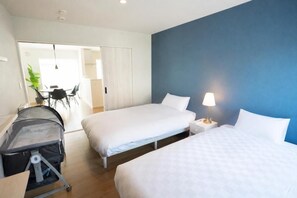 Ein Hotelzimmer mit zwei Betten, einem Schreibtisch, einem Stuhl, einer Lampe und einem Kinderwagen.