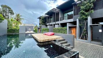 A modern building with a swimming pool, a wooden deck, and a red pillow.