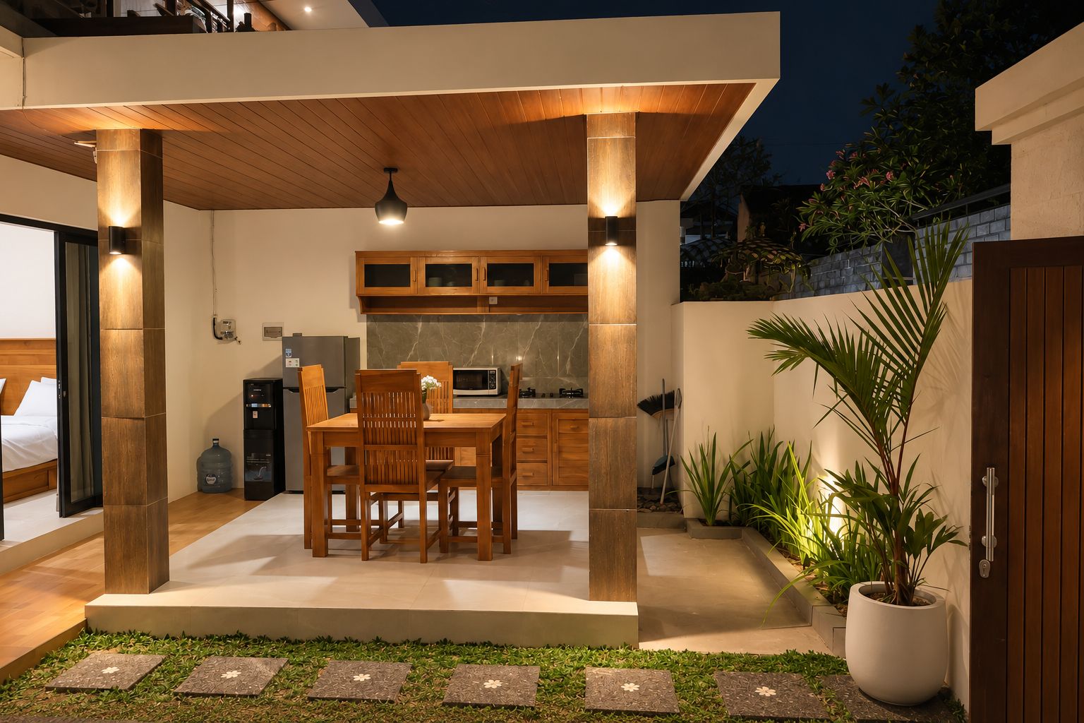 Un área de comedor al aire libre y moderna con una mesa y sillas de madera, una cocina al fondo y una planta en maceta.