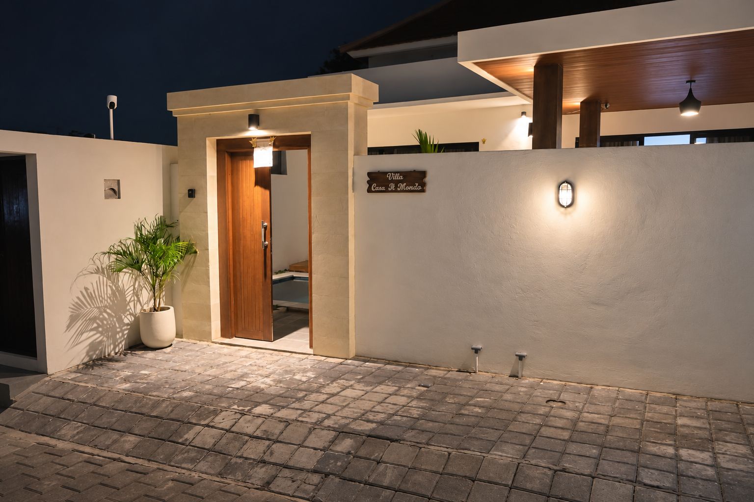 A modern villa entrance with a wooden door, a potted plant, and a sign indicating the villa name.