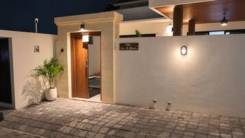 A modern villa entrance with a wooden door, a potted plant, and a sign indicating the villa name.
