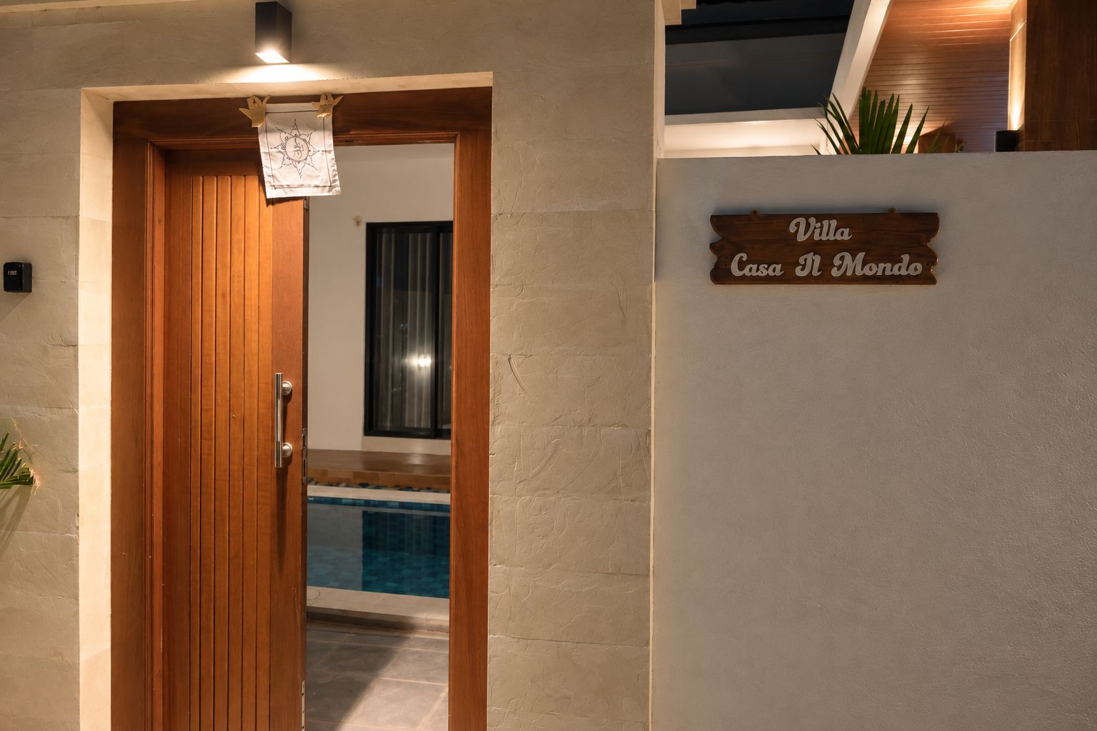 En trädörr leder in till poolområdet, och ovanför dörren finns en skylt med texten ”Villa Casa del Mondo”.