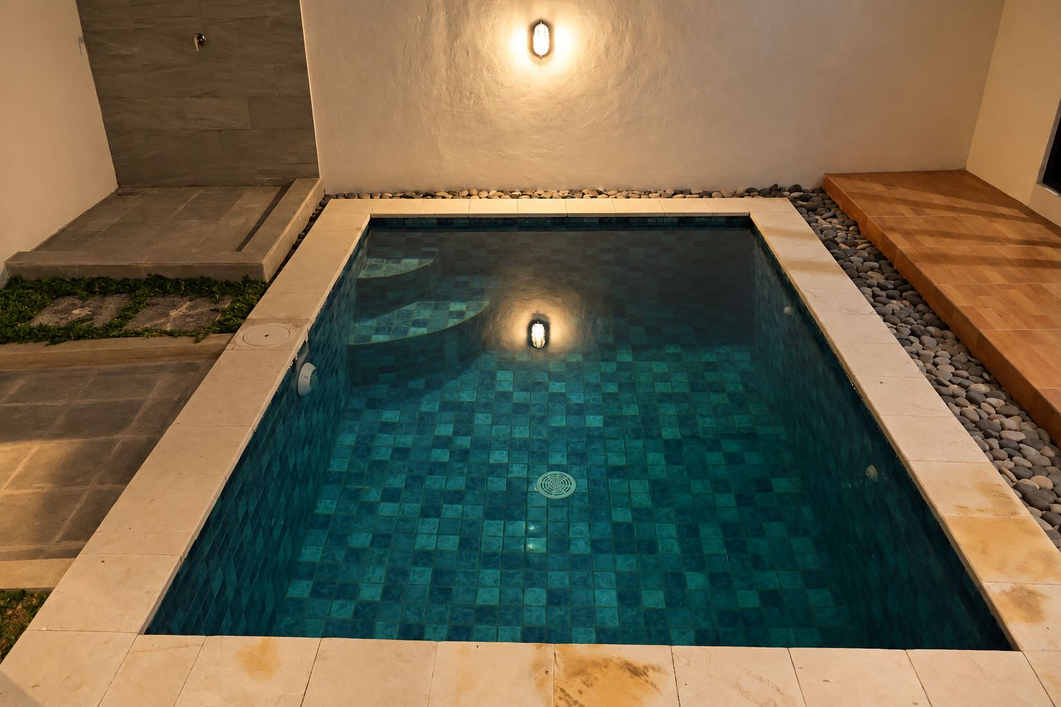 Una piscina rectangular con suelo de baldosas, rodeada por un borde de piedra y una cubierta de madera.