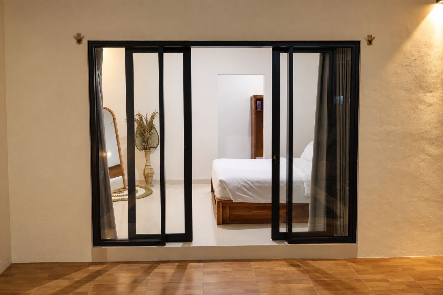 A room with a sliding door leading to a bed and a small table with a vase.