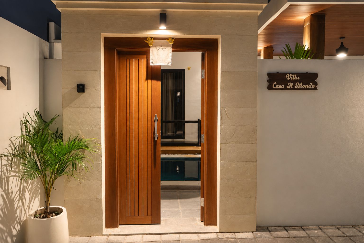A hotel entrance with a wooden door, a sign reading 'Villa Casa Il Mondo,' and a potted plant beside it.