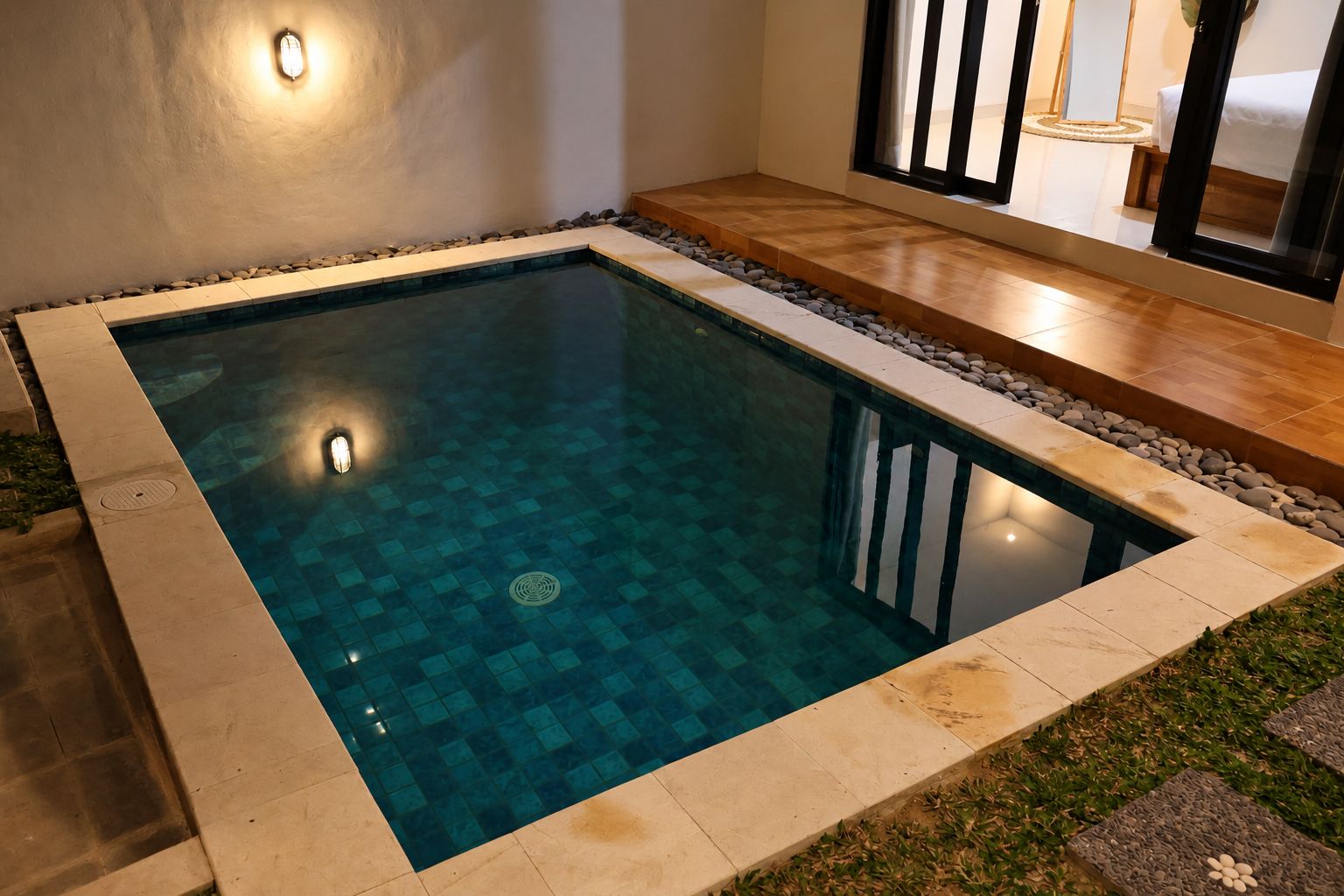 A rectangular swimming pool with a tiled edge, surrounded by a stone border and a wooden deck.