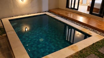 A rectangular swimming pool with a tiled edge, surrounded by a stone border and a wooden deck.