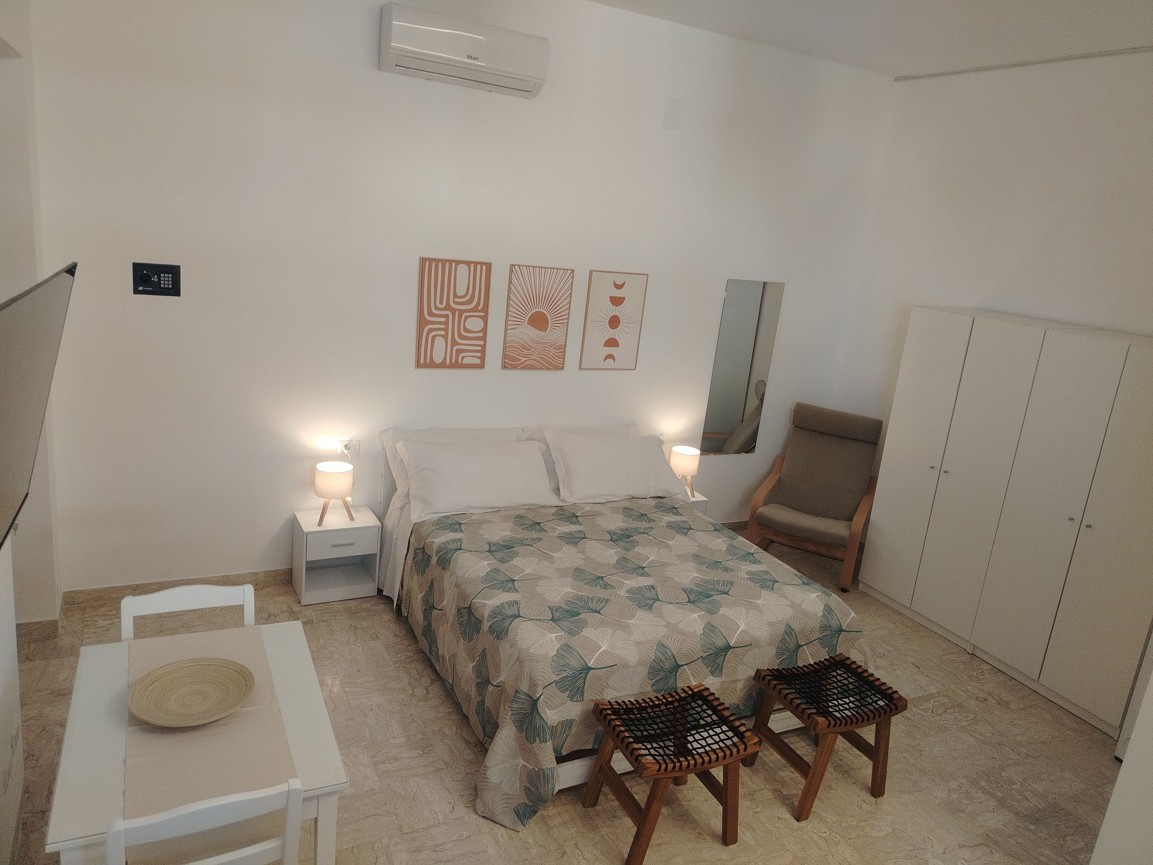 Una camera da letto con un letto, lampade sui comodini, una poltrona, un tavolo e un armadio.