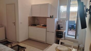 Una cucina compatta con mobili bianchi, un lavello e un frigorifero. È presente un tavolo da pranzo apparecchiato con piatti, posate e bicchieri.