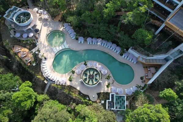 An aerial view of a resort with a large irregularly shaped pool surrounded by lounge areas and a circular water feature.