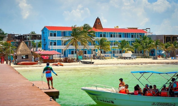 A beachfront hotel with a red-roofed building, a pier, and a boat with passengers. - El Faro by OOL Hotels (Isla Holbox)