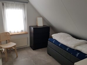 A bedroom with a bed, a dresser, a chair, and a window with curtains. - Strand4you Zeeland Village (Scharendijke)