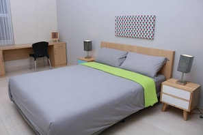 Un dormitori amb un llit, taules de nit, escriptori, una cadira i una obra d'art penjada a la paret.