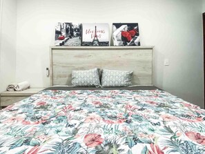 Ein Schlafzimmer mit blumigem Überwurf auf dem Bett, einem Holzkopfteil und drei gerahmten Bildern an der Wand.