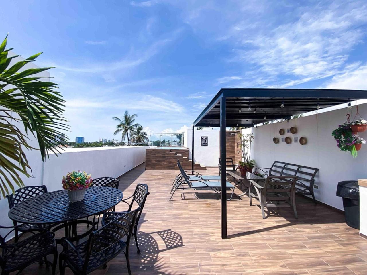 Una terraza en la azotea con un área de estar techada, una mesa con sillas y plantas en macetas.