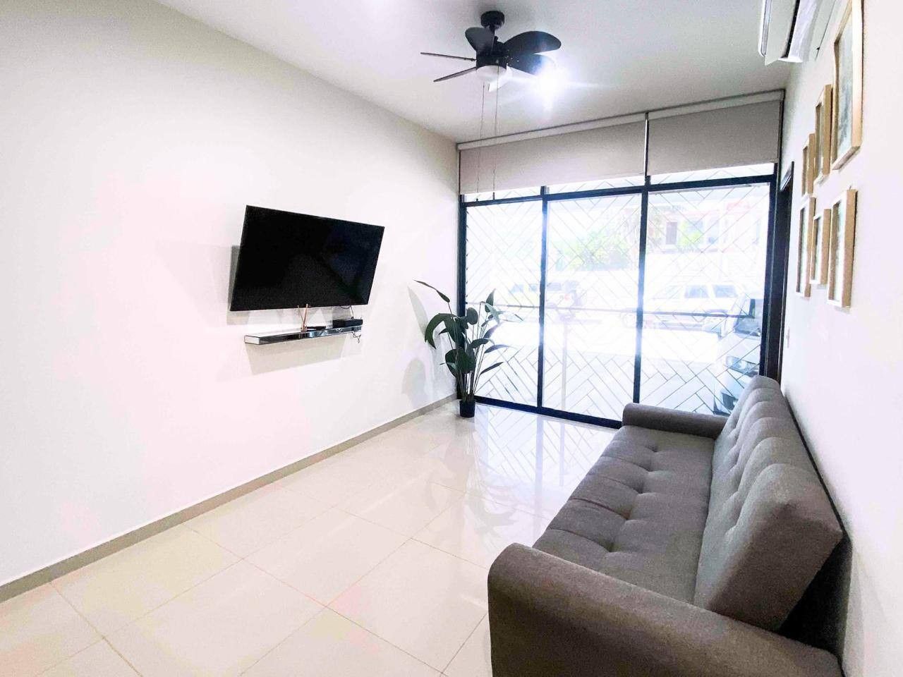 Una sala de estar con un televisor de pantalla plana montado en la pared, un sofá y una planta en maceta.
