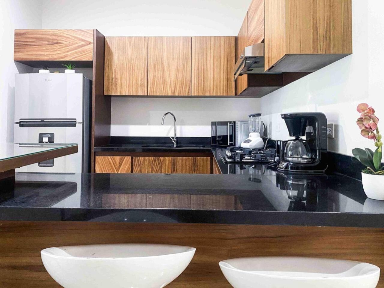 Una cocina moderna con armarios de madera, encimera negra, cafetera y una planta en maceta.