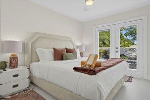 Ein Schlafzimmer mit einem großen Bett, Nachttischlampen, einem Beistelltisch und Blick durch eine Glastür.