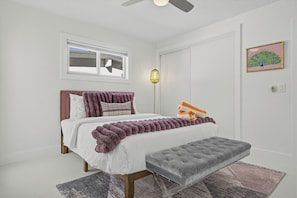 A bedroom with a bed, a bench, a window, a door, a ceiling fan, and a wall-mounted light fixture. - Pool + Hot Tub + Game Room | Mtn Views + Fire Pit | The Royal Palms (Palm Springs)
