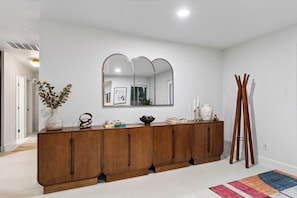 A modern interior with a wooden console table, a large mirror, and a wooden coat rack. - Pool + Hot Tub + Game Room | Mtn Views + Fire Pit | The Royal Palms (Palm Springs)