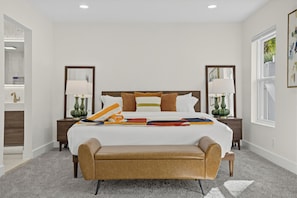 A modern hotel room with a large bed, two bedside tables, a bench, and a view of greenery outside. - Pool + Hot Tub + Game Room | Mtn Views + Fire Pit | The Royal Palms (Palm Springs)