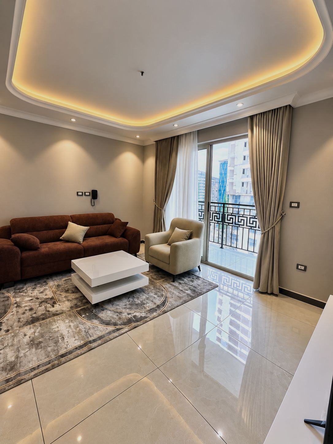 A modern living room with a sofa, armchair, and coffee table, a large window with curtains, and a balcony with a railing.
