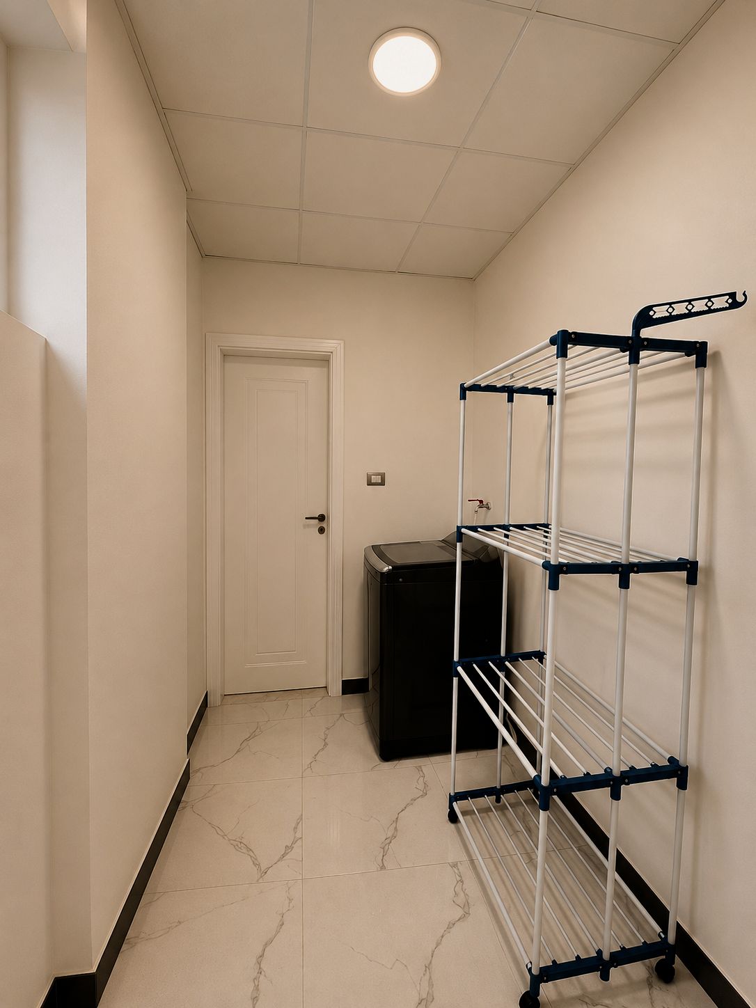 A hallway with a white door, a black appliance, and a metal drying rack against the wall.