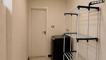 A hallway with a white door, a black appliance, and a metal drying rack against the wall.
