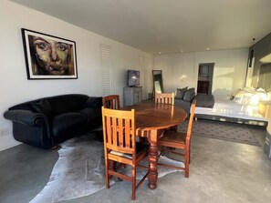 A modern living room with a round wooden dining table, a black leather sofa, and a large painting on the wall. - Flip Flops Villa Luxury Studio in Yzerfontein (Yzerfontein)