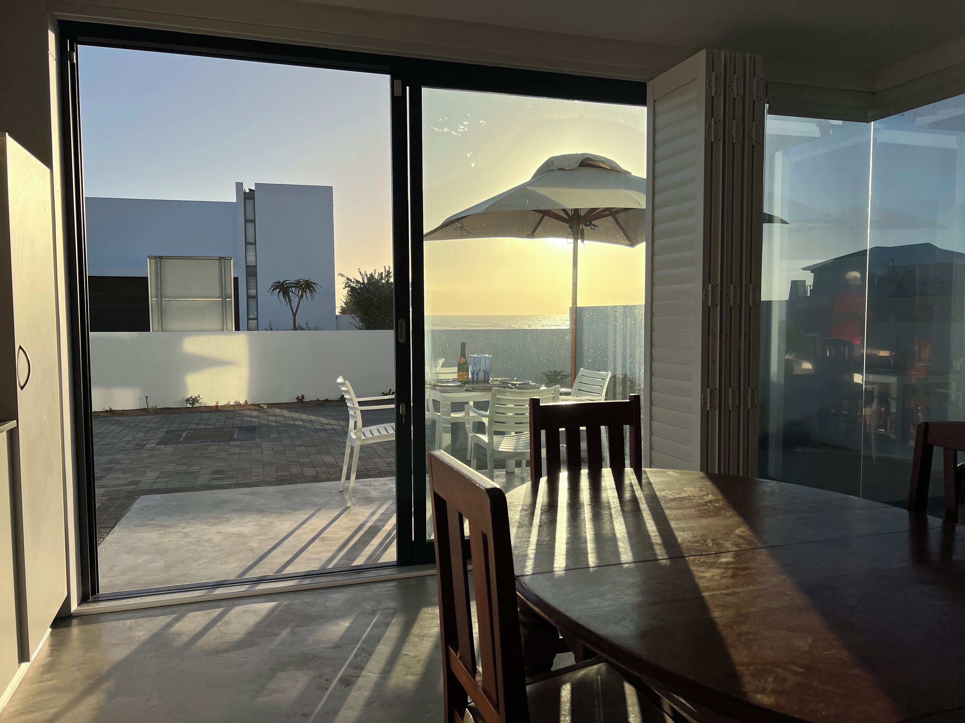 Un intérieur moderne avec une porte-fenêtre coulissante donnant sur un patio extérieur équipé d’une table, de chaises et d’un grand parasol.