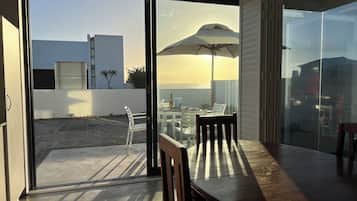 Un intérieur moderne avec une porte-fenêtre coulissante donnant sur un patio extérieur équipé d’une table, de chaises et d’un grand parasol.