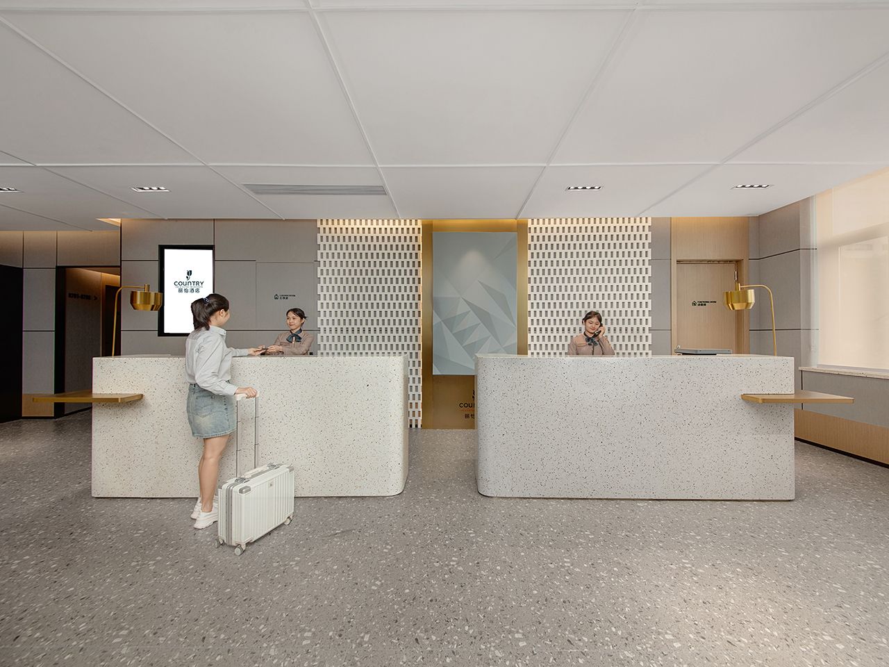Un espace d’accueil comprenant deux comptoirs de réception, une personne debout près de l’un des comptoirs, et un mur orné d’un motif géométrique.